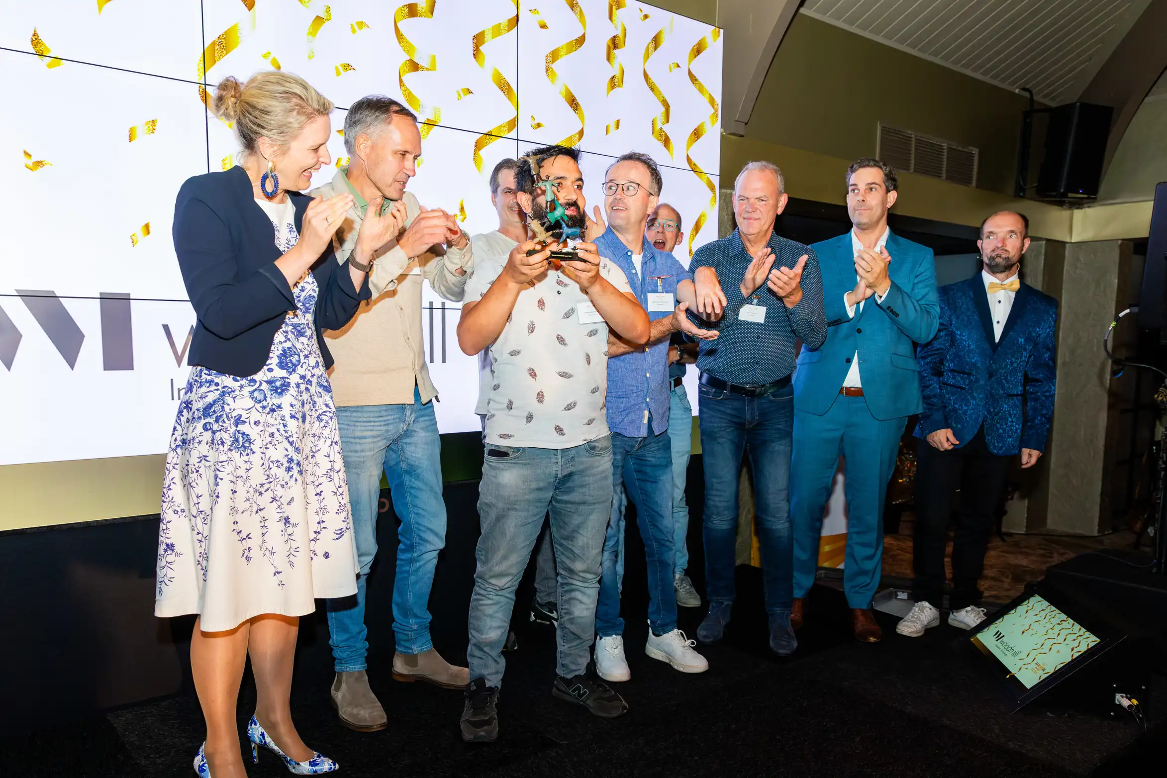 winnaar op de foto met trofee in handen en andere genodigde eromheen